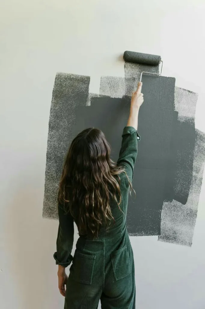 A woman painting walls with neutral colors to refresh her home affordably.